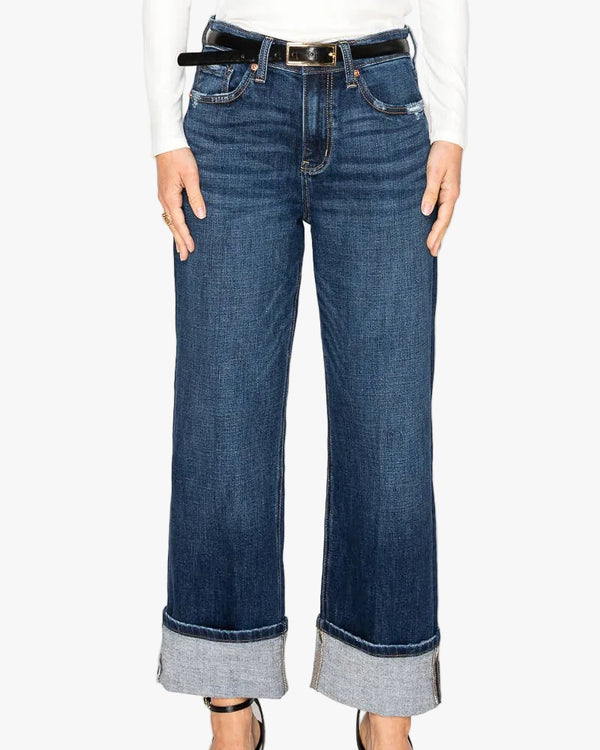 Woman in a white shirt wearing a pair of straight legged jeans with the bottoms cuffed on a white background.
