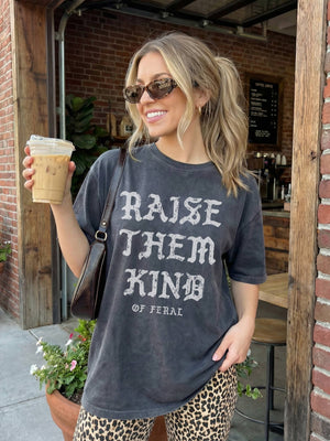 Woman holding a coffee cup outside a brick building, wearing a t-shirt with text.