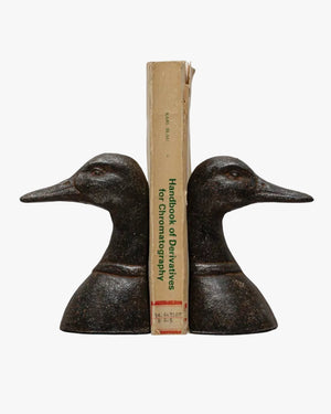 A pair of black cast metal duck head bookends with a book placed in between them, on a white background.