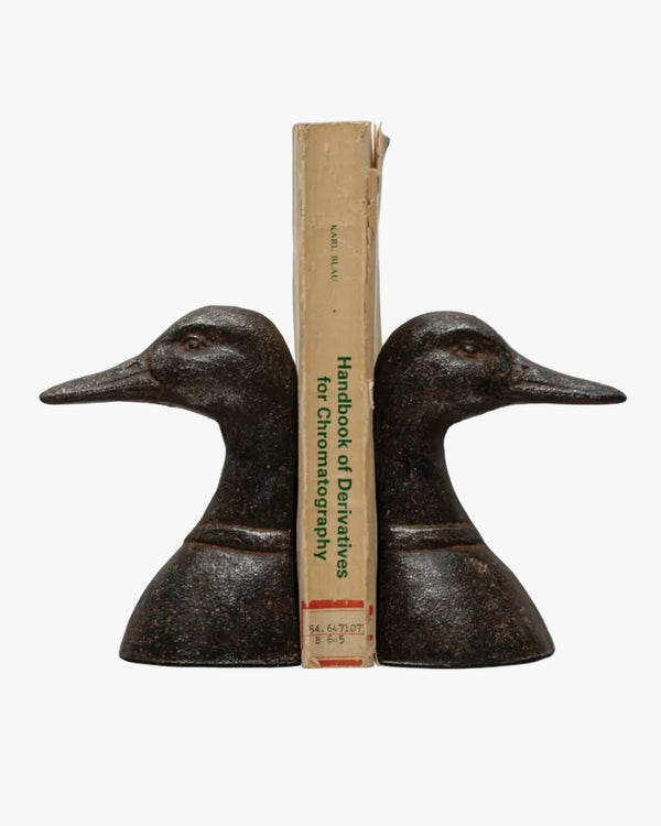 A pair of black cast metal duck head bookends with a book placed in between them, on a white background.