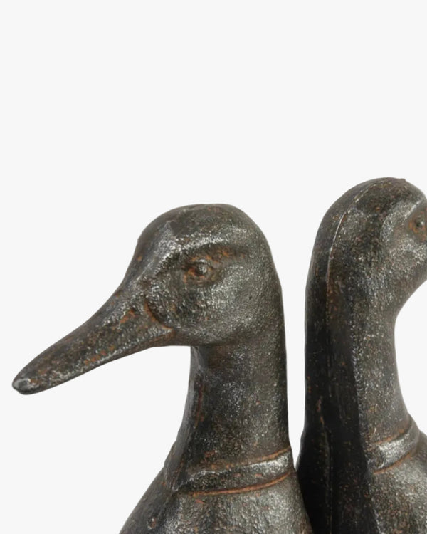 A pair of black cast metal duck head bookends on a white background.