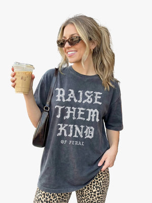 Woman holding a coffee cup outside a brick building, wearing a t-shirt with text.