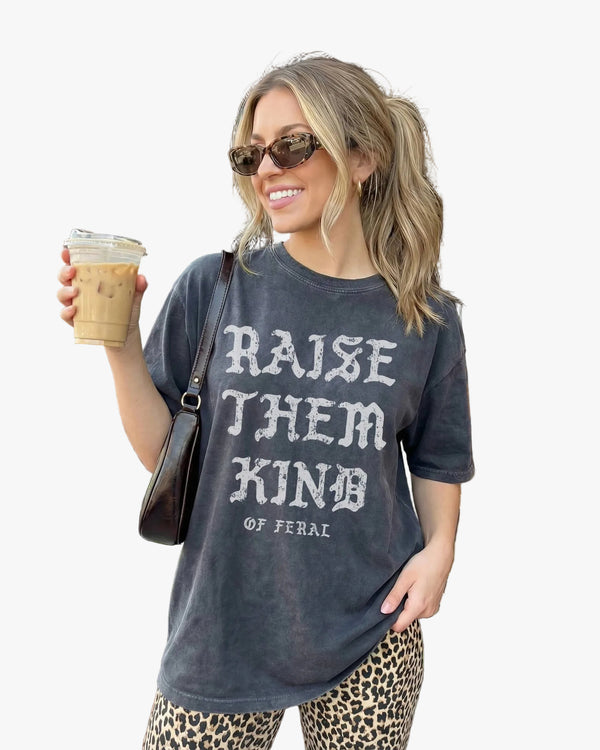 Woman holding a coffee cup outside a brick building, wearing a t-shirt with text.